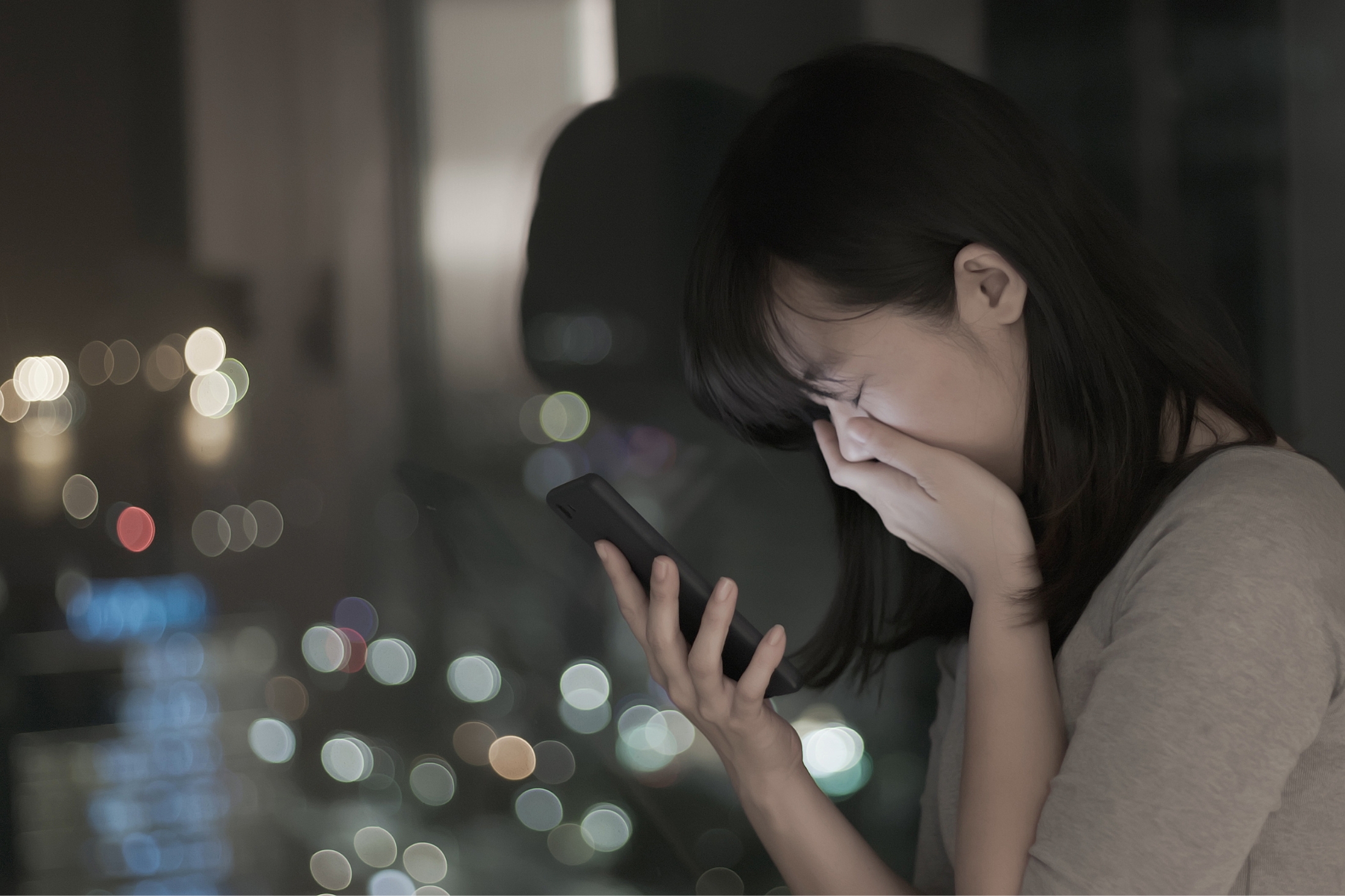 A distressed woman holds her left hand over her mouth while holding a cell phone in her right hand
