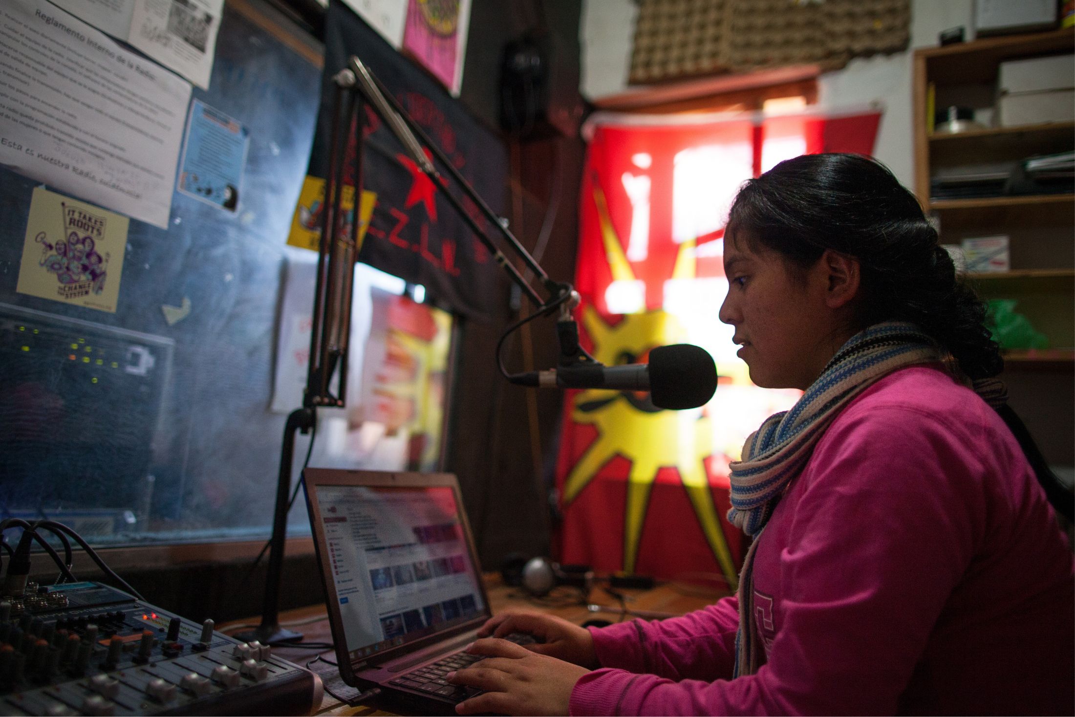 A young women of the Lenca nation in Honduras sits at a radio console and speaks into a microphone while working on a laptop